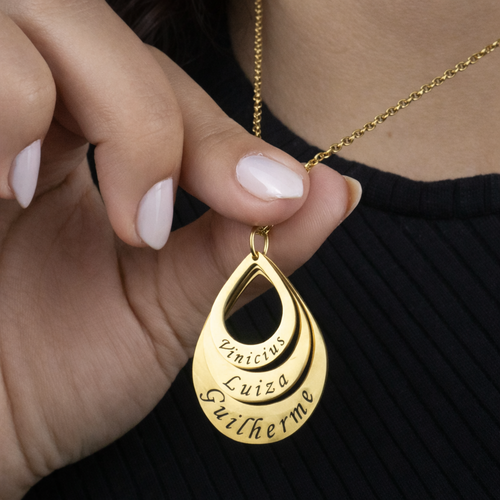 Colar_Gota_de_Amor_dourado_com_nomes_personalizados_detalhe_da_peca_segurada_para_evidenciar_o_brilho_e_acabamento