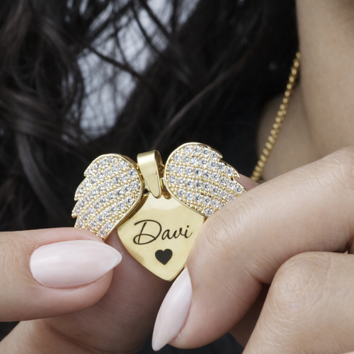 Colar_Asas_de_Anjo_dourado_com_coracao_personalizado_gravado_com_nome_e_asas_cravejadas_sendo_exibido_no_pescoco