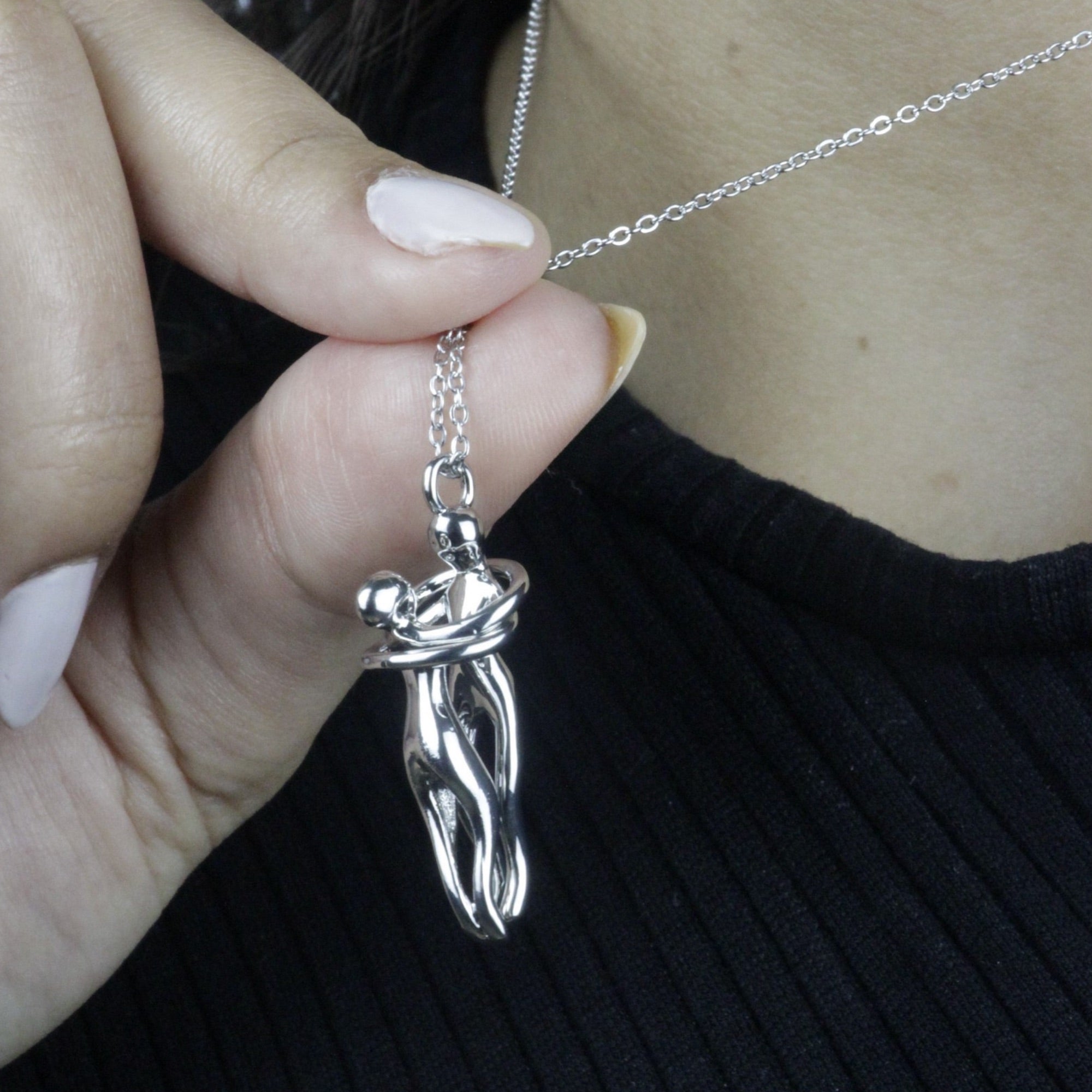 Colar Abraço Eterno prateado com pingente em formato de casal se abraçando, modelo segurando a peça para destacar os detalhes do design