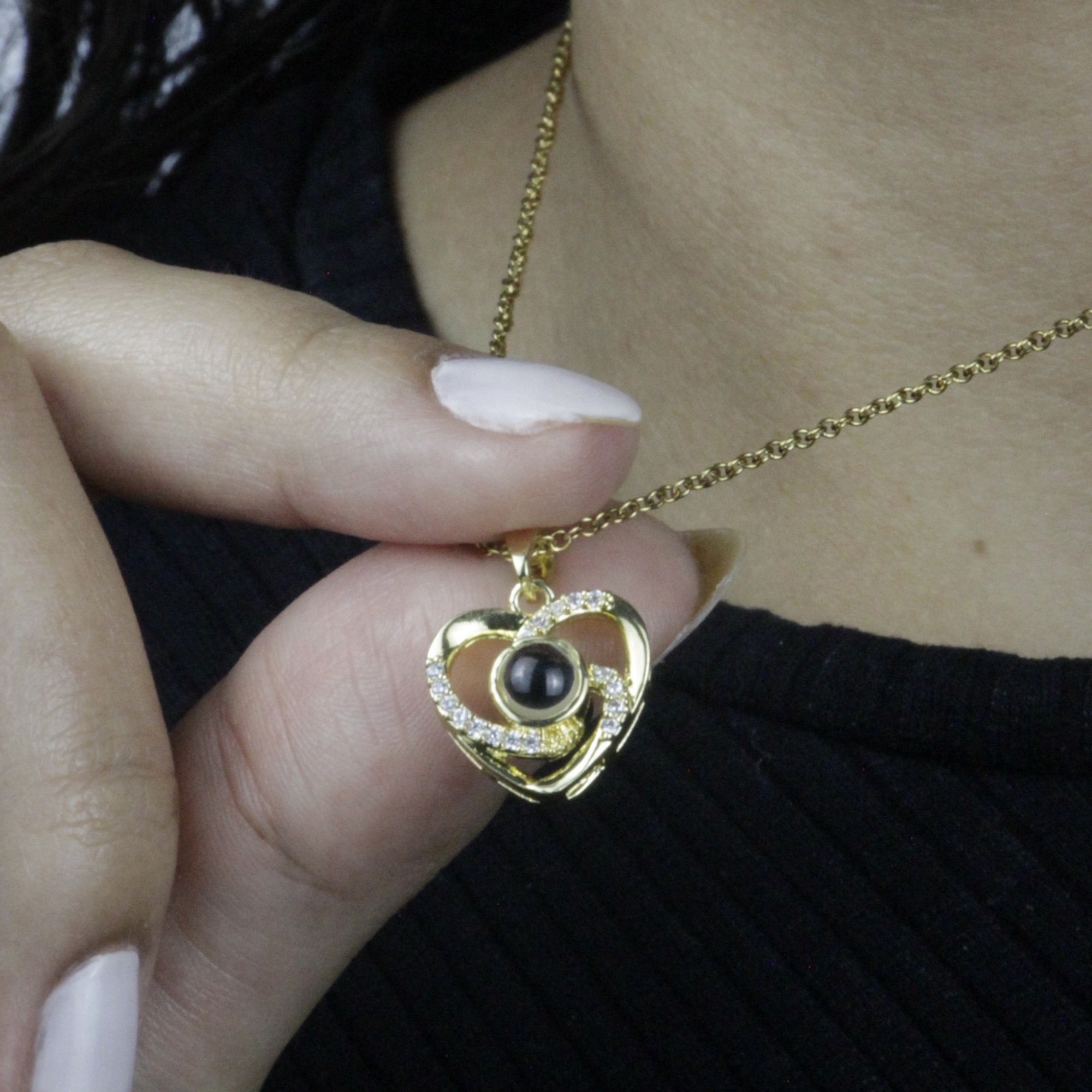 Colar_Eu_te_amo_dourado_em_formato_de_coracao_com_pedra_central_e_detalhes_cravejados_sendo_segurado_no_pescoco