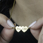 Colar_Meus_Coracoes_dourado_com_dois_coracoes_gravados_com_nomes_detalhe_da_peca_sendo_segurada_para_destacar_o_acabamento