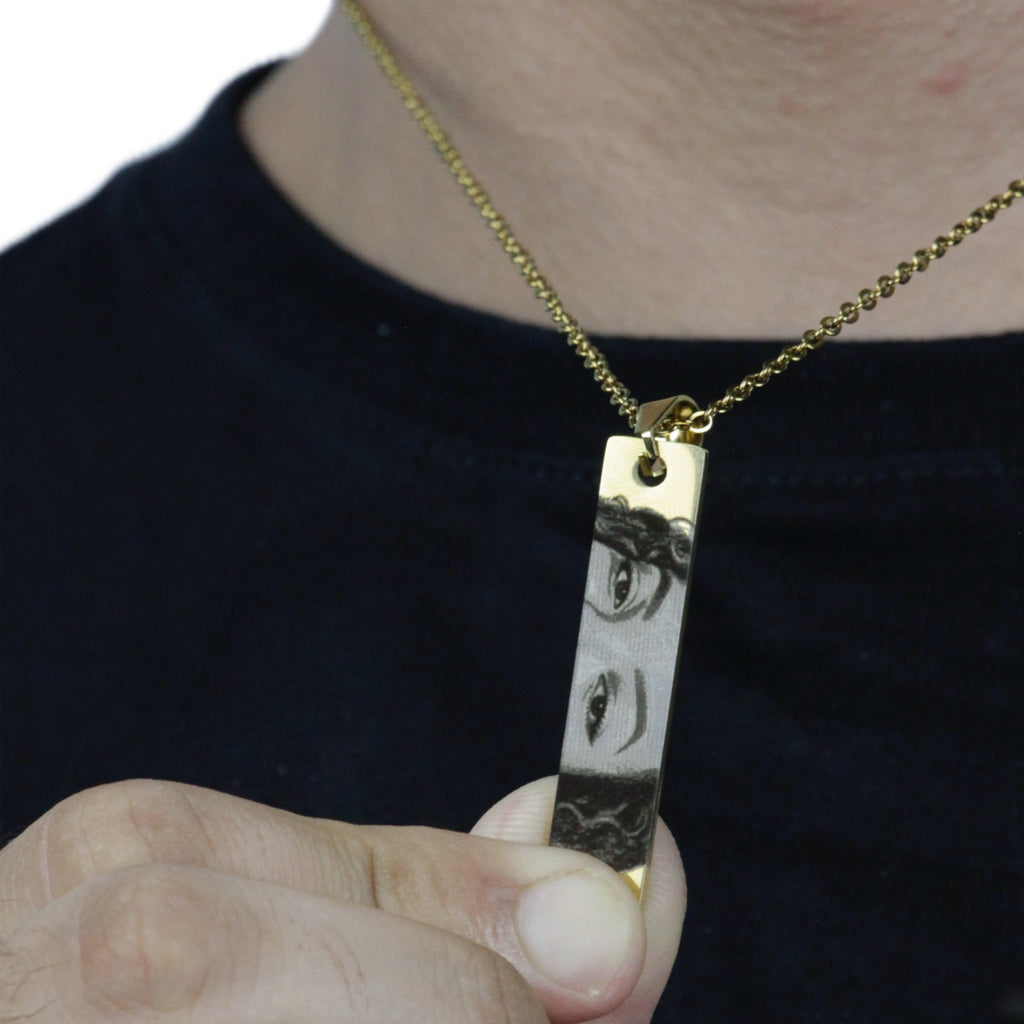 Colar_do_Olhar_dourado_com_pingente_retangular_gravado_sendo_segurado_pelo_modelo