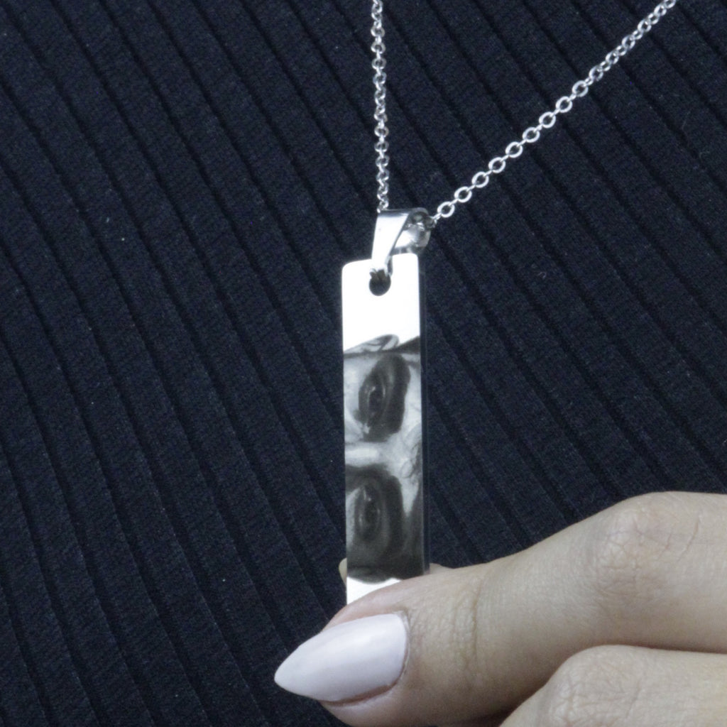 Colar_do_Olhar_prata_com_pingente_retangular_gravado_sendo_segurado_pela_modelo