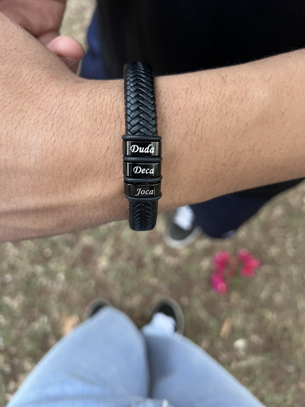 Pulseira masculina de couro trançado preto no pulso com contas gravadas Duda, Deca e Joca