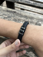 Pulseira de couro trançado preta no pulso masculino com nomes Duda, Deca e Joca